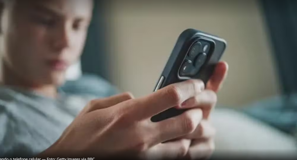 Aluno segurando um celular em uma sala de aula, representando o uso restrito de dispositivos móveis nas escolas após a aprovação do projeto pelo Senado.